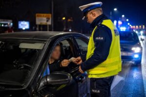 Policjant sprawdza dokumenty kierowcy podczas nocnej kontroli drogowej.