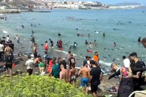 Migranci zgromadzeni na plaży i w wodzie u wybrzeży Ceuty po przekroczeniu granicy z Marokiem.